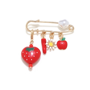 Detail of gold safety pin brooch with strawberry, daisy, apple charms and a white pearl