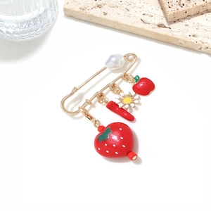 Detailed close-up of fruit and chili enamel charms on a gold safety pin with white pearl