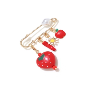 Close-up of golden pin with strawberry, chili, and daisy charms in pastoral style