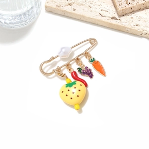 Detail of a gold safety pin brooch with a pearl and colorful fruit vegetable charms