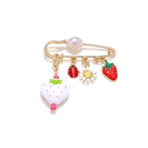 Detail of gold safety pin brooch with strawberry, daisy, and ladybug charms