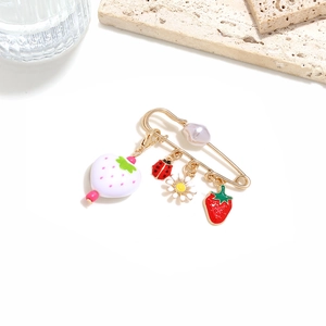 Detail of gold safety pin brooch with strawberry charms, ladybug, and daisy flower