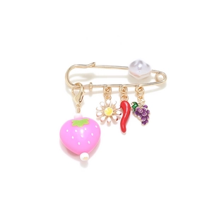 Golden safety pin brooch with strawberry, daisy, chili, and grape charms on white background