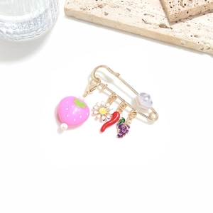 Detailed macro view of gold safety pin brooch with strawberry and daisy charms