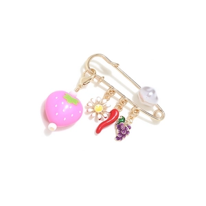 Close-up of gold safety pin brooch with strawberry, daisy and chili pendants