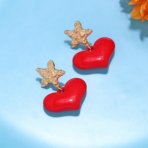 Close-up of golden textured star studs with glossy red heart pendants on blue background
