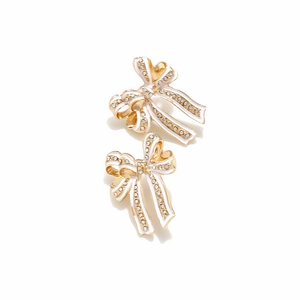 Detailed macro view of gold-plated bow earrings with white enamel and sparkling rhinestones