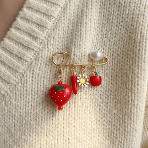 Golden safety pin brooch with strawberry pepper and daisy charms on knit sweater