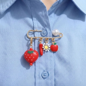 Pastoral style gold safety pin brooch with strawberry, chili, and daisy charms on a blue shirt