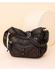 Macro detail of black leather crossbody bag featuring multiple zippers and vintage buttons