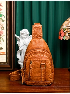 Detail view of a vintage brown washed leather chest bag with dual zippers on a wooden table