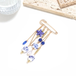 Detail showing golden star brooch with ceramic beads and fringe chains on stone surface
