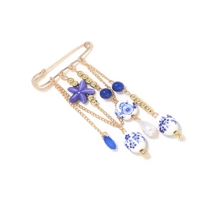 Detail of a ceramic starfish brooch with blue floral beads and golden tassel chains