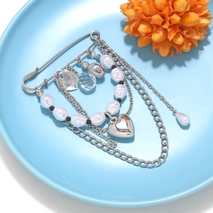 Detail of silver multi-layer chain brooch with heart pendant and pearls on blue plate