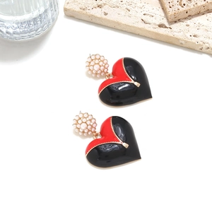 Détail de boucles d'oreilles cœur en émail avec perles et design de zip doré