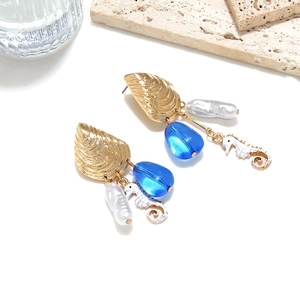 Detail of nautical earrings featuring golden shells, blue beads, and seahorse charms