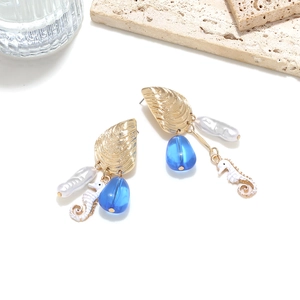 Detailed macro shot of asymmetrical seashell and seahorse earrings with baroque pearls