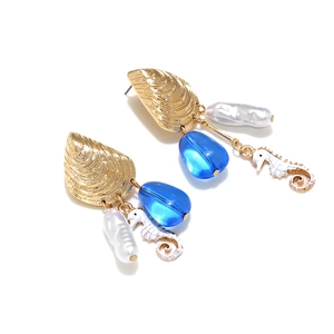 Ocean theme earrings with golden shells, white seahorses and blue beads on white background