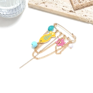 Detailed shot of golden safety pin brooch with enamel fish, pink flower and blue beads