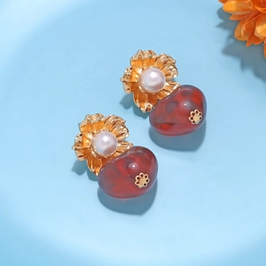 Macro detail of gold flower earrings with white pearls and deep red resin teardrop pendants