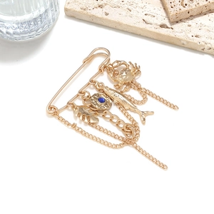Macro detail of a gold safety pin brooch featuring crab, tropical fish, and blue gemstone