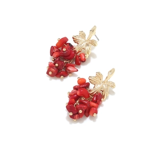 Detail of bohemian drop earrings with golden leaves and red stone clusters