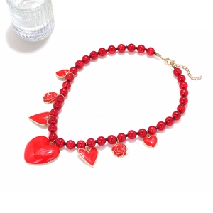 Detail of red beaded necklace with heart pendants and rose charms on a white surface