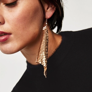 Close-up of long gold sequin tassel earrings on model with shimmering metallic mesh