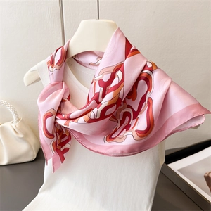 Close-up of pink silk square scarf with abstract geometric patterns on a white hanger