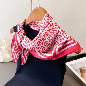 Detail of red leopard print satin scarf tied on a blue vest with elegant accessories
