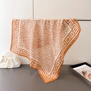 Detail of warm orange leopard print silk scarf with Greek key border hanging on a metal rod