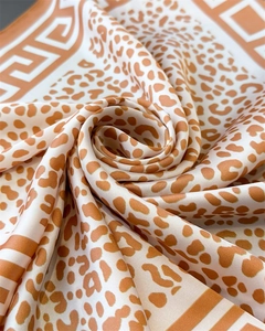 Close-up of leopard print satin silk scarf featuring Greek meander borders in orange tones