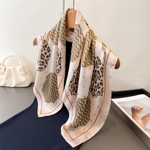 Elegant leopard and teal wave print square silk scarf hanging on a wooden hanger