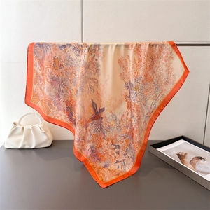 Detail eines Satin-Halstuchs mit tropischem Blumenmuster und orange-cremefarbener Textur