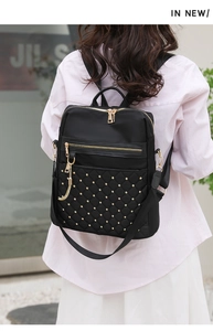 Rear view of a black quilted backpack with gold studs shown on a model's back