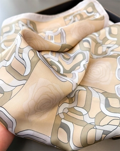 Close-up of elegant silk scarf with beige geometric prints and floral patterns in a gift box