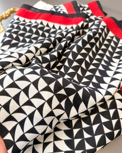 Detail of herringbone pattern silk scarf with red border and geometric crescent print