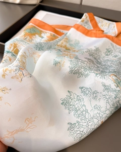 Detailaufnahme eines bedruckten Seidentuchs mit orangem Saum und Naturmotiv