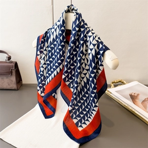Elegant geometric silk scarf with blue triangles and orange borders hanging on a white rack