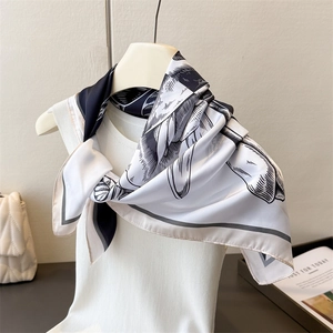 Detail of silk-like scarf with black leaf print tied on a white knitted top