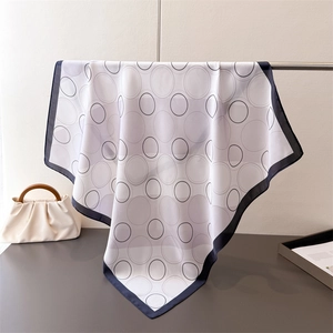 Detail of geometric pattern silk scarf draped on metal rack with a beige handbag