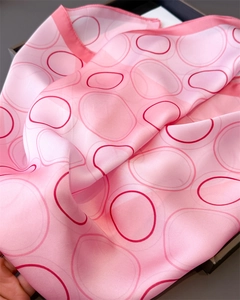 Detail of pink silk scarf with red geometric pattern and soft satin texture in a box