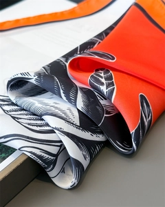Detailed close-up of orange floral silk scarf fabric showing soft satin texture