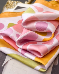 Gros plan d'un foulard carré en soie aux motifs géométriques rose et vert au drapé élégant