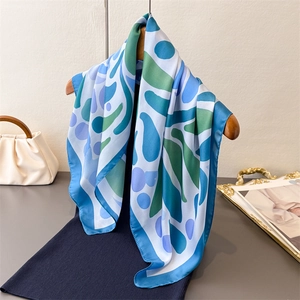 Foulard en soie avec imprimé abstrait bleu et vert drapé sur un cintre avec robe