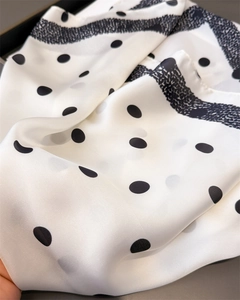 Gros plan détaillé montrant la texture satinée et les pois noirs sur ce foulard en soie