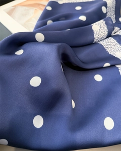 Vue macro d'un foulard en soie bleu marine à pois avec bordure florale blanche délicate