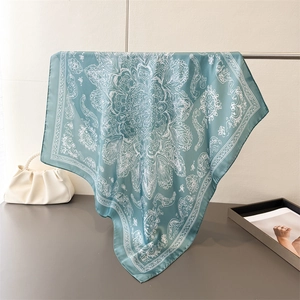 Elegant teal silk square scarf with white mandala patterns hanging on a metal display rack