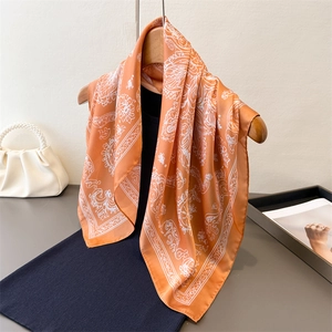 Elegant orange silk square scarf with vintage floral patterns hanging on a wooden hanger