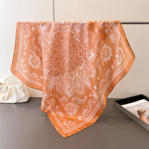 Detail of vibrant orange silk scarf with white mandala pattern hung on a metal rack